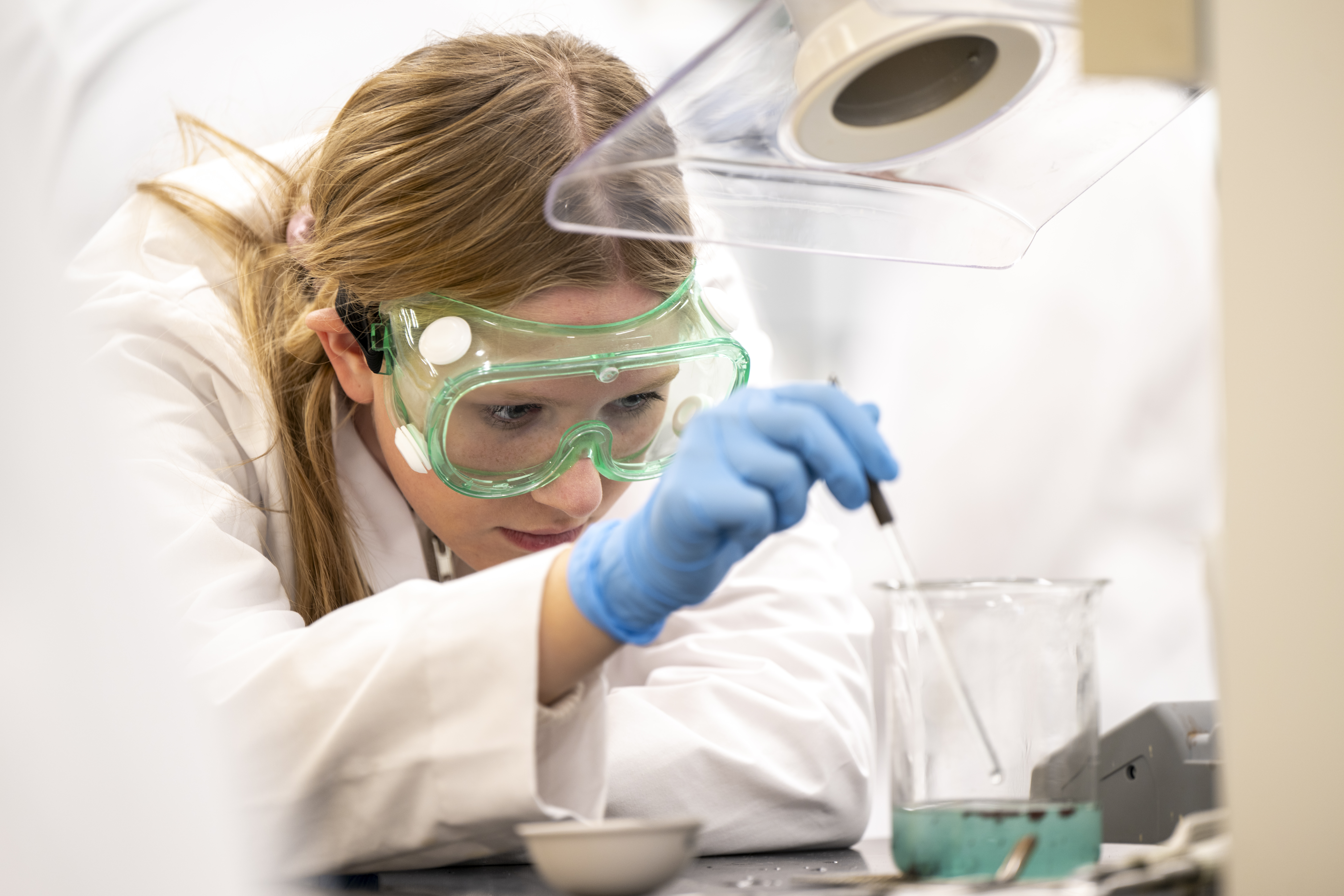 Student wearing safety head gear holding pipette and mixing blue solution